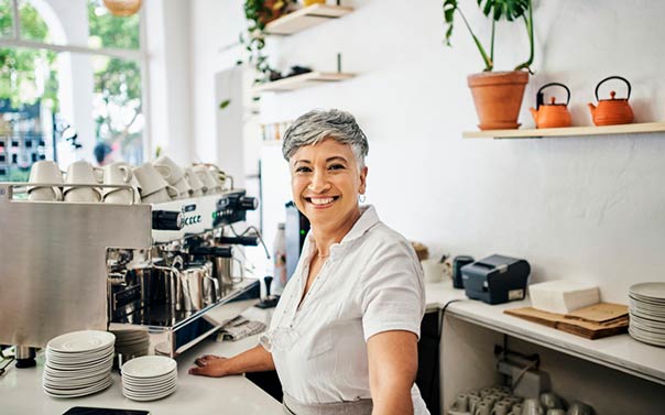 mature female coffee shop owner smiling behind the counter